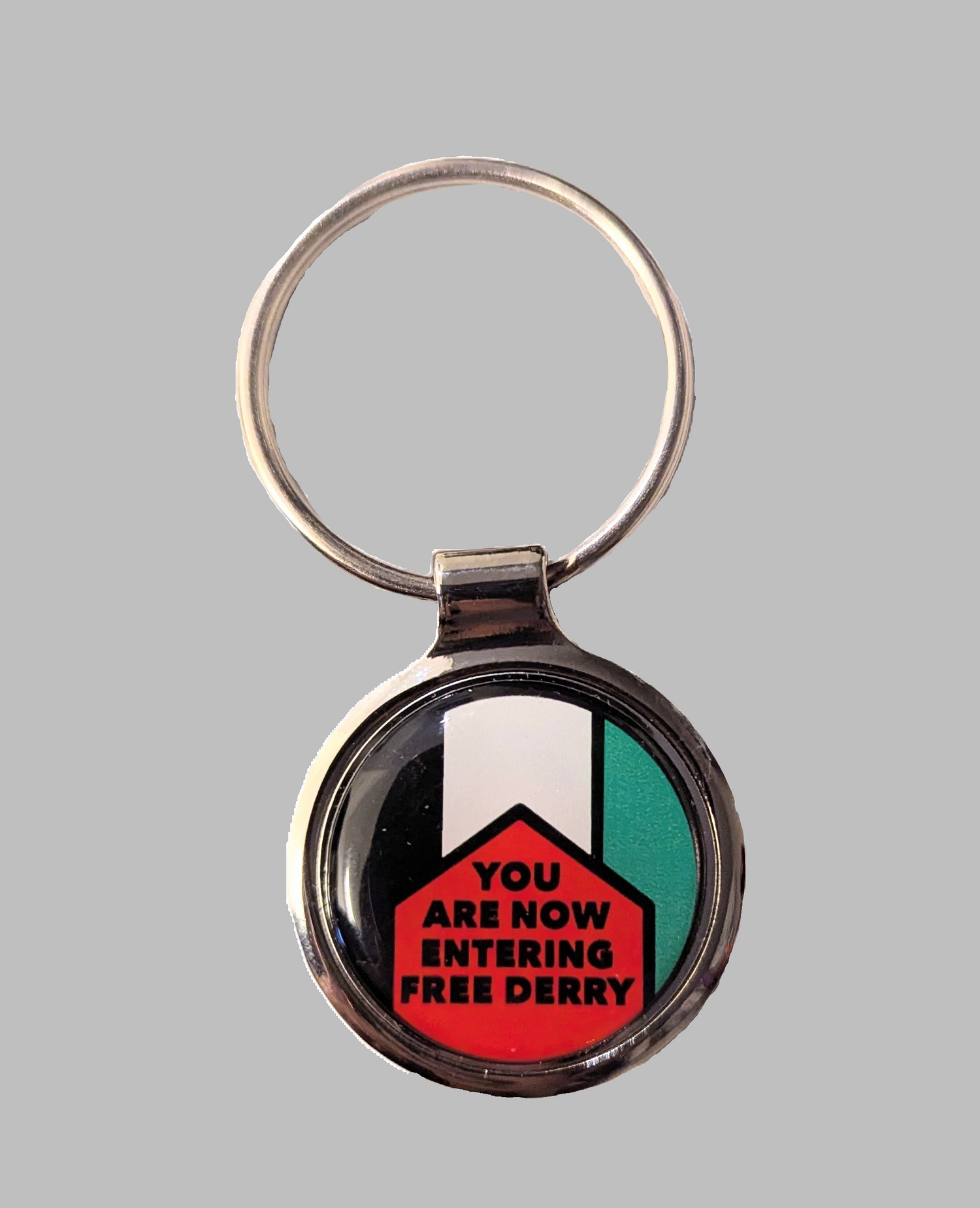 Round silver keyring with “You Are Now Entering Free Derry” design over the colours of the Palestinian flag.